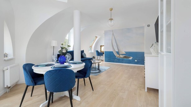 A dining area with a round table, blue chairs, and a sailboat mural on the wall.