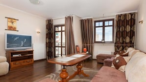 A living room with a wooden coffee table, a television, a sofa, and a window with curtains.