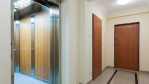A hallway with a wooden door, a metal elevator, and a tiled floor.