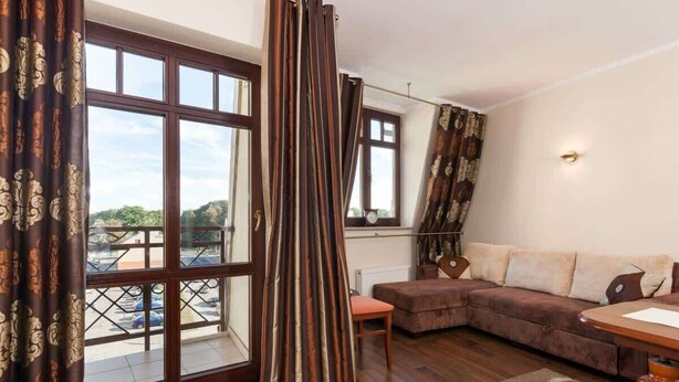 A living room with a brown sectional sofa, a wooden coffee table, and a view of a parking lot through large windows.