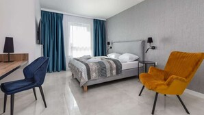 A modern hotel room with a bed, a desk, a chair, and a lamp.