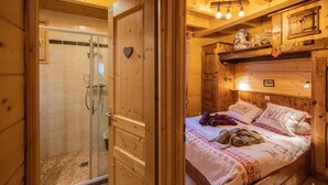 Een houten blokhut van binnen met een douche, een bed met een beddegoed met patroon en houten kasten.