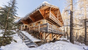Een houten chalet met balkon, omgeven door sneeuw en bomen.