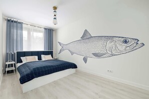 A bedroom with a bed, a ladder, a wall mural of a fish, and a window with curtains. - Bright Apartment with Balcony | 200 m from the Beach (Świnoujście)