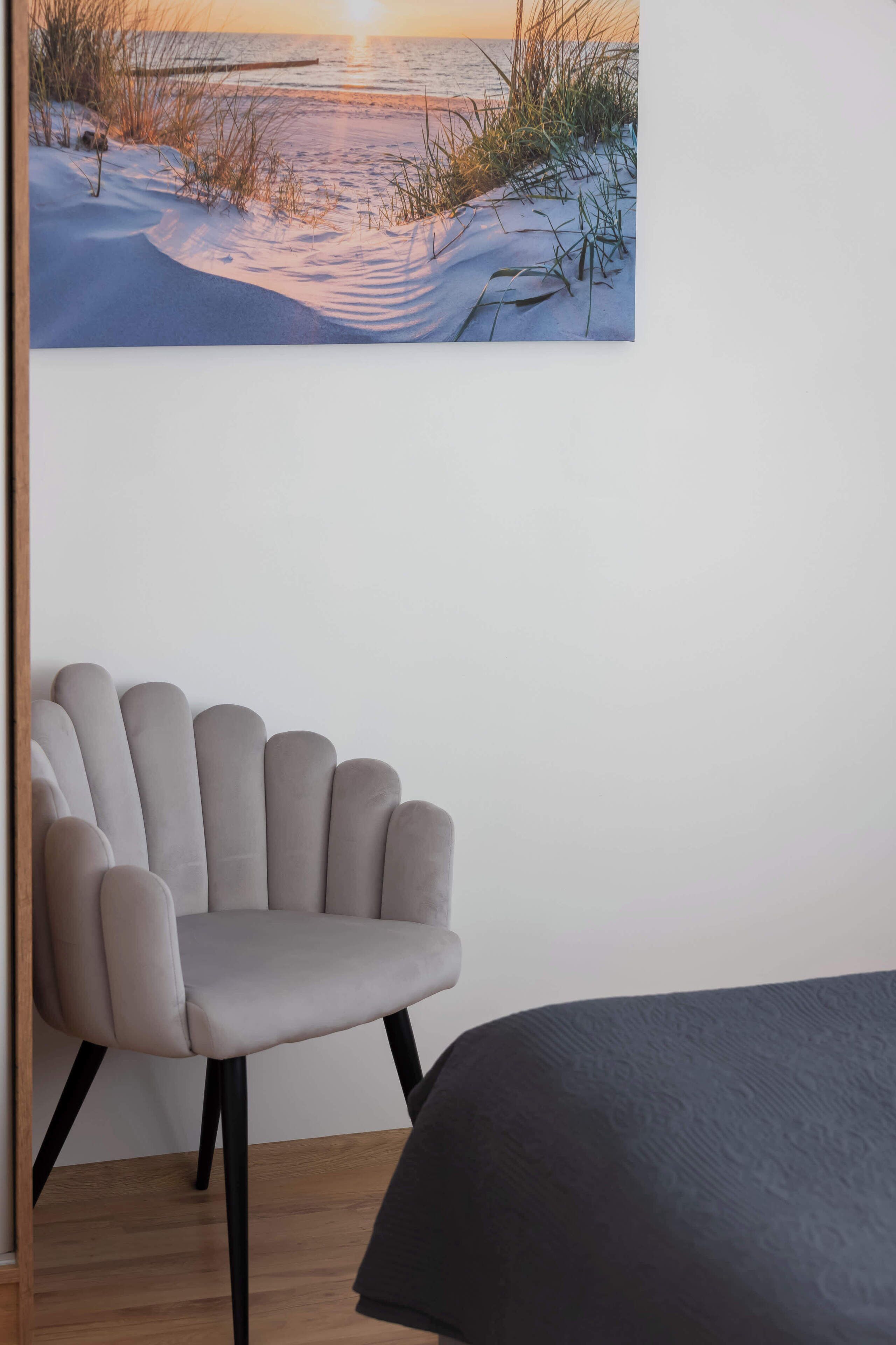 Een kamer met een bed, een stoel en een schilderij van een strandgezicht.