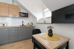 Une cuisine moderne avec des meubles gris, un plan de travail en bois, un micro-ondes noir et un téléviseur noir fixé au mur.