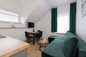 Une petite pièce moderne, dotée d’un bureau en bois, d’un canapé vert, d’une table à manger avec des chaises et d’un téléviseur fixé au mur.