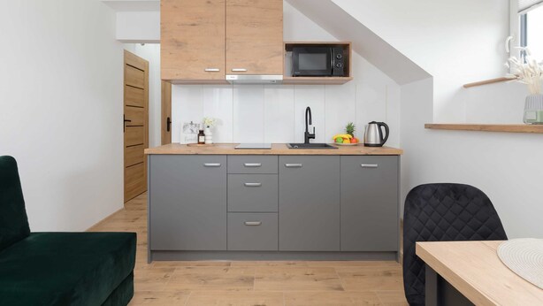 A modern kitchen with grey cabinets, a wooden countertop, a microwave, and a black chair.