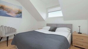 A bedroom with a bed, a chair, a nightstand, and a painting on the wall.