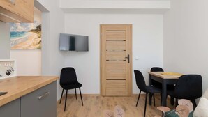 A room with a wooden door, a flat-screen TV, a dining table with chairs, and a bed with decorative leaves.