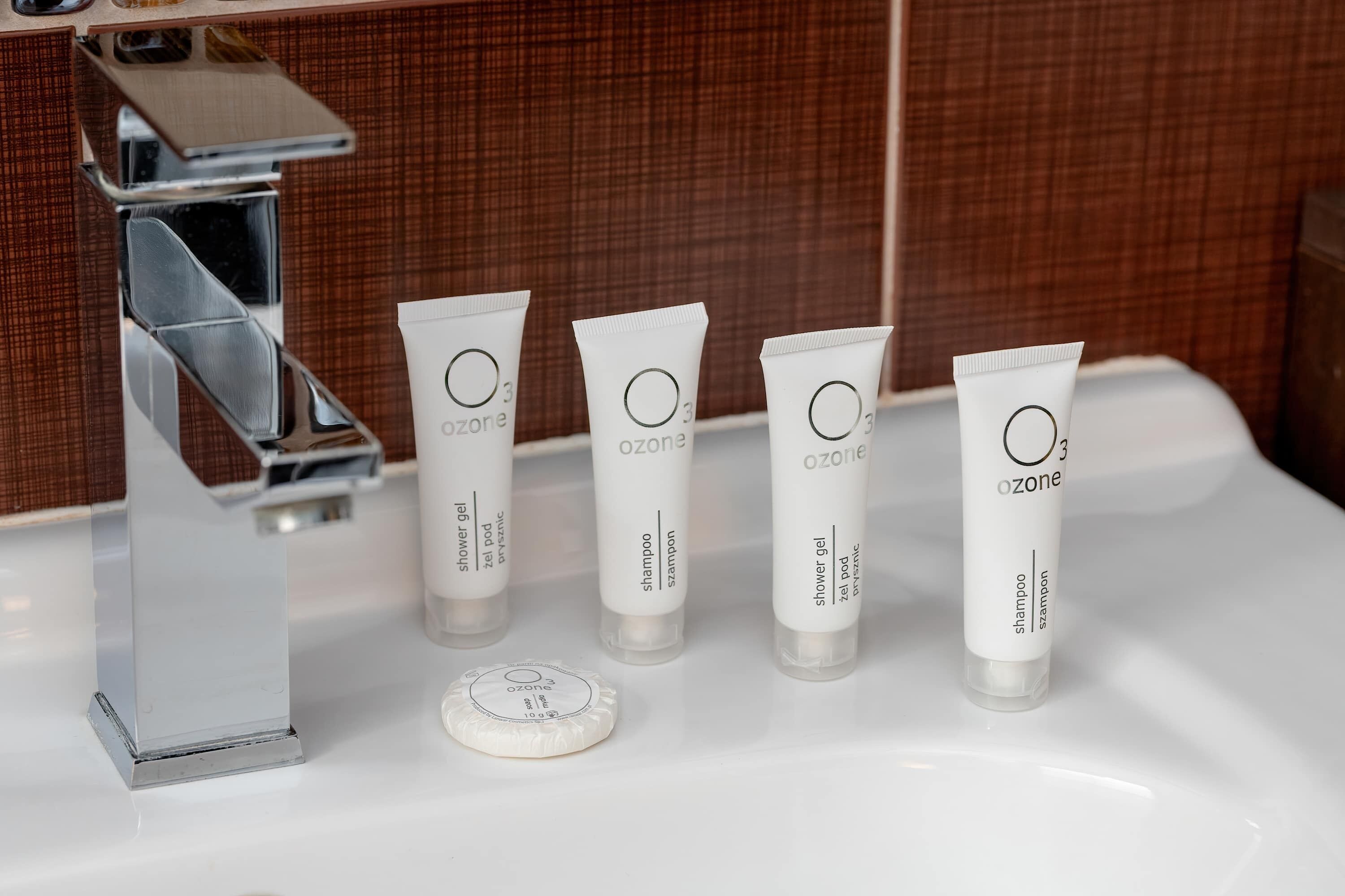 A bathroom sink with four ozone shampoo and shower gel tubes, a white cap, and a chrome faucet.
