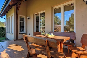 A patio with wooden furniture, a table with a tray of fruits, and a view of the outdoors through large windows.