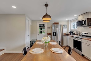 A modern kitchen with a wooden dining table set for four, equipped with a stainless steel refrigerator, microwave, and stove. - Downtown Saratoga Home w/ Yard & Patio (Saratoga Springs)