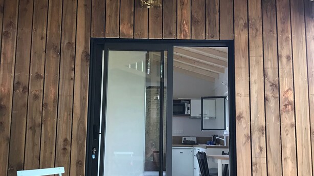 A wooden exterior with a sliding glass door leading to a kitchen area.