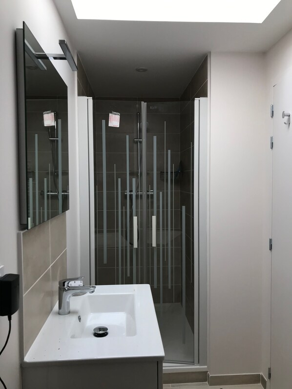 Une salle de bain moderne avec un lavabo blanc, un grand miroir et une douche à parois de verre.