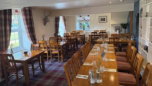 A dining area with wooden tables and chairs, a stone wall with a deer head decoration, and a window with plaid curtains. - the Star Inn (Weaverthorpe)
