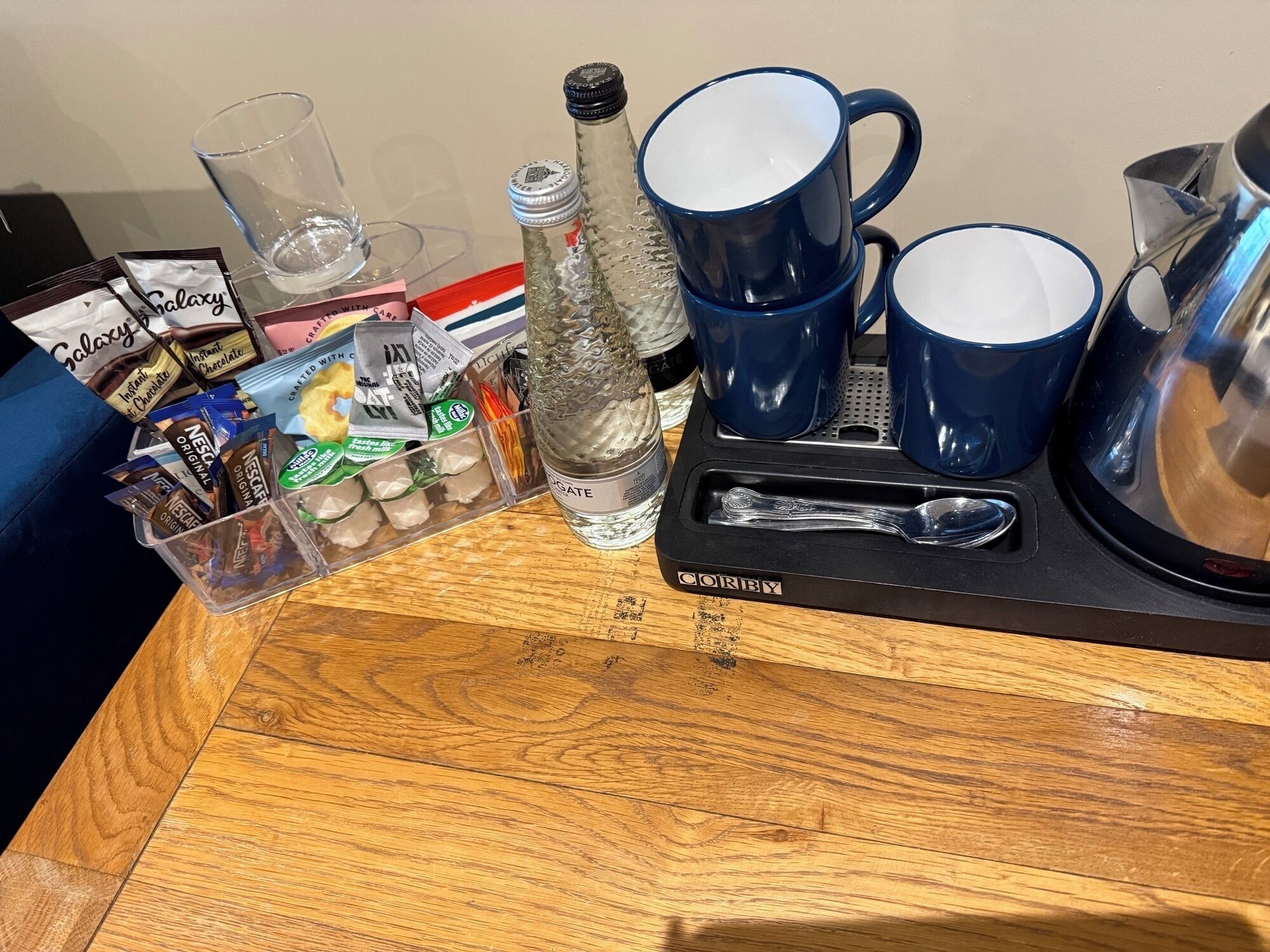 Un plateau contenant une bouteille, deux tasses bleues, un verre et divers emballages de collations, le tout posé sur une table en bois.