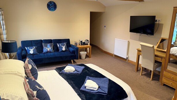 A bedroom with a large bed, a blue sofa, a wooden desk, and a television. - the Star Inn (Weaverthorpe)