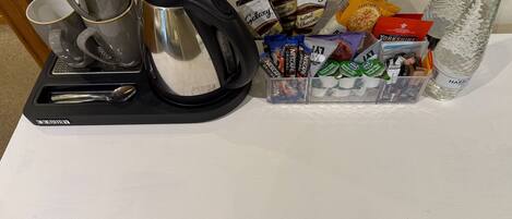 A coffee maker, cups, and a snack dispenser on a table.
