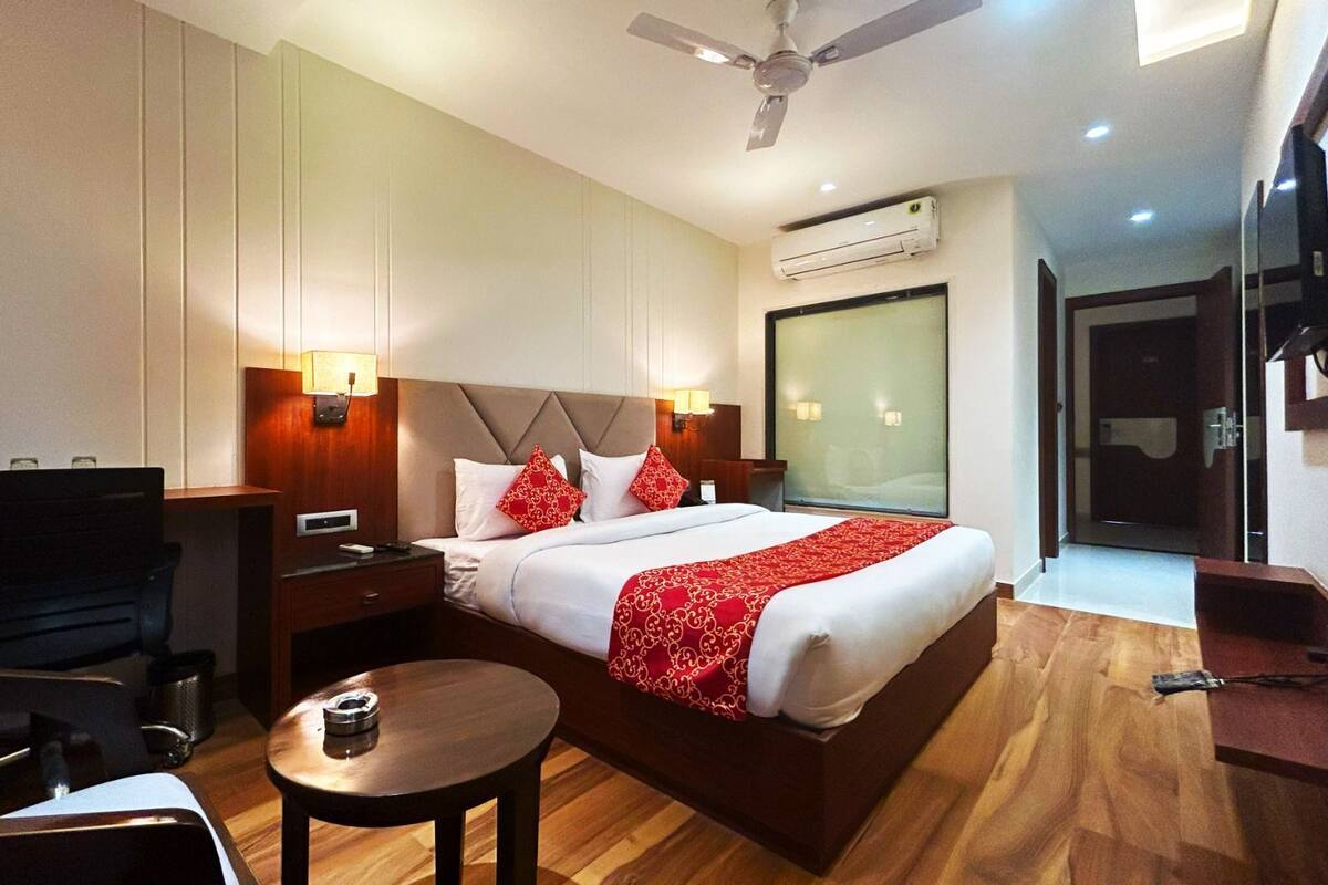 Ein Hotelzimmer mit Bett, Nachttischen, Schreibtisch, Stuhl, rundem Tisch, Deckenventilator und Klimaanlage.