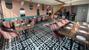 Un restaurante con sillas a rayas, mesas dispuestas con platos y vasos, y un suelo con estampado geométrico.