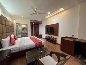 A modern hotel room with a large bed, a TV mounted on the wall, a desk, and a seating area with a glass table. - Hotel The crystal Park  (Gwalior)