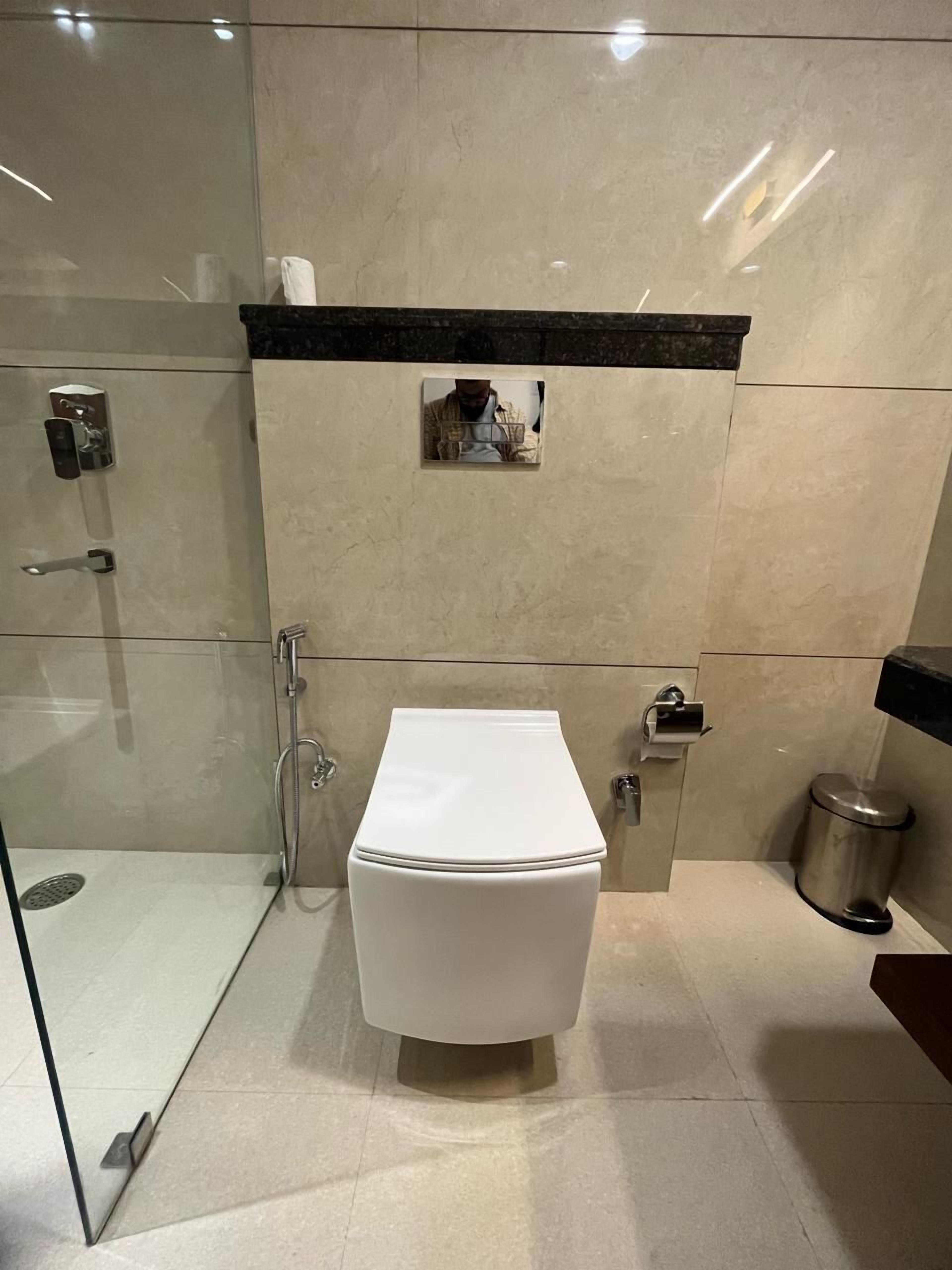 A modern bathroom with a glass-enclosed shower, a white toilet, and a trash can.