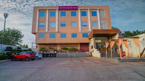 Un hotel de varios pisos llamado "The Crystal Park", con fachada moderna, un acceso cubierto y un estacionamiento con varios coches.