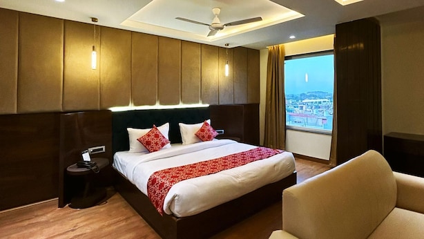 Habitación de hotel con una cama grande, un ventilador de techo y vistas a un paisaje urbano a través de la ventana.