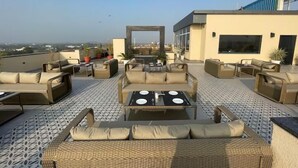 Una terraza en la azotea con mobiliario exterior, vistas de la ciudad y un edificio moderno al fondo.