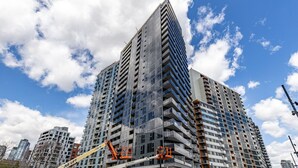 A high-rise building with multiple floors, construction cranes, and a clear blue sky with clouds.