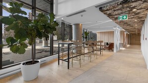 A modern interior with large windows, a central seating area with tables and chairs, and a ceiling with a unique pattern.