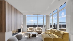 A modern living room with a large window, a sofa, two armchairs, and ottomans.