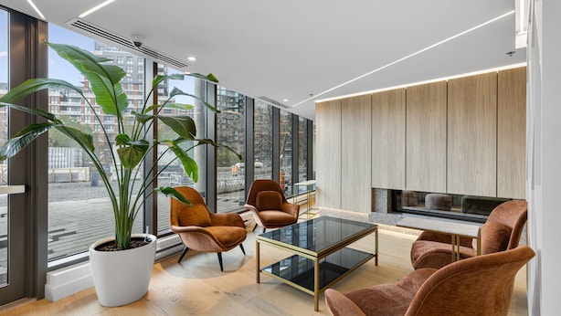 A modern living room with large windows, a potted plant, and a flat-screen TV.