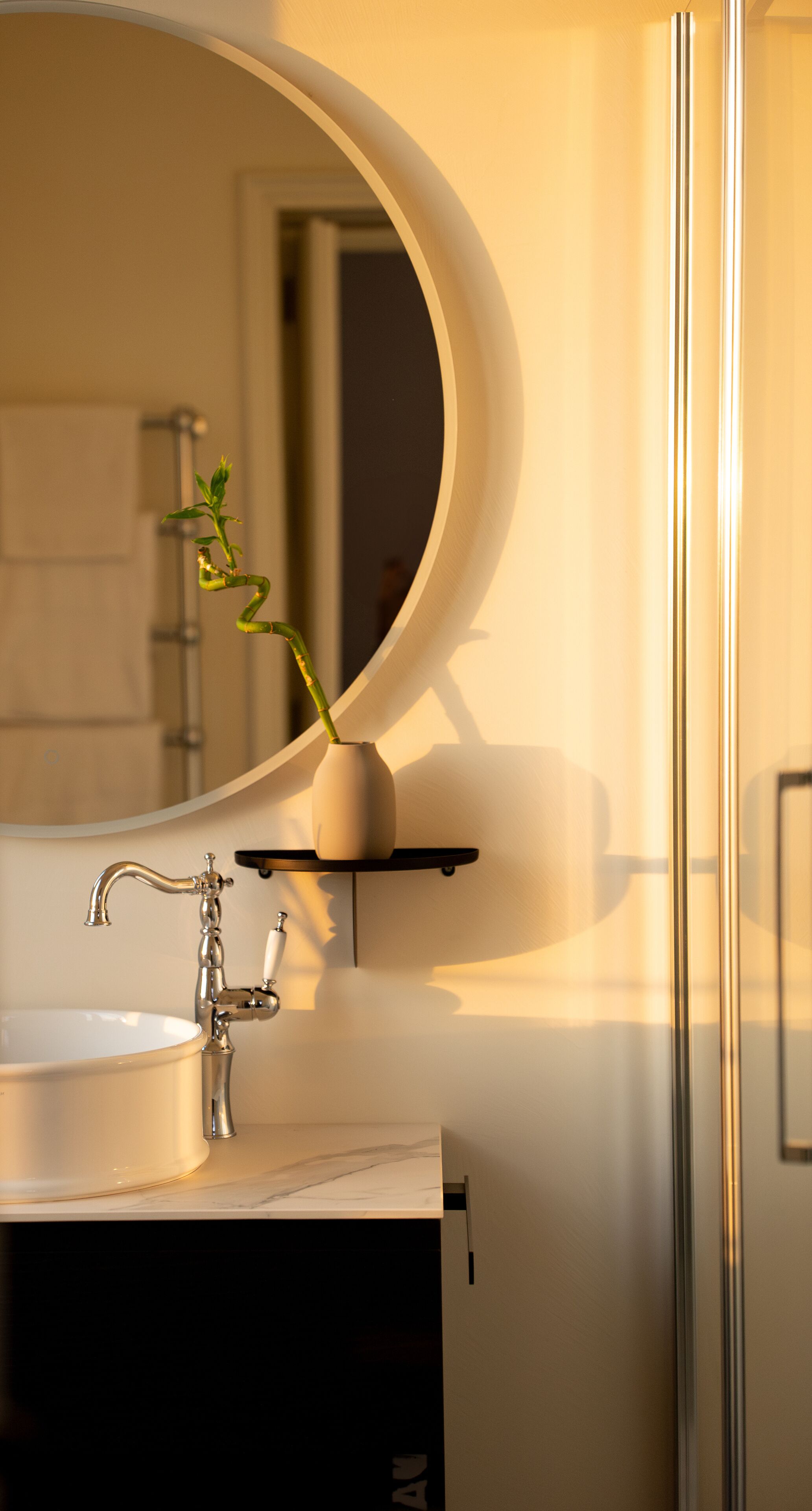Une salle de bain avec un miroir rond, un lavabo blanc et un robinet moderne.