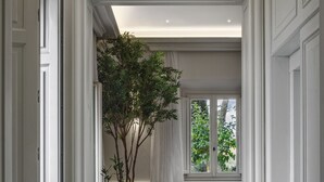 A hallway with white doors, a large potted plant, a window with white curtains, and a dark floor with a compass design. - One Belvedere Tuscany (Poggibonsi)