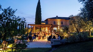 An outdoor dining area with tables and chairs, surrounded by a stone building and trees. - One Belvedere Tuscany (Poggibonsi)