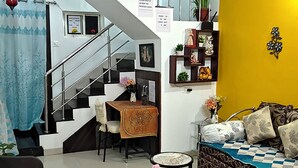 A living room with a staircase, a sofa, a dining table, and a wheelchair.