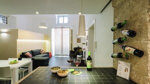 A modern kitchen with a dining table, two bowls of fruit, and wine glasses.