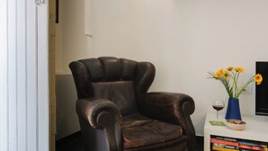 A leather armchair, a vase with flowers, a wine glass, and a stack of books on a white table.
