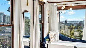 A room with a large window, a blue sofa, a small table with a plant, and a view of a cityscape. - Top 2 Floors Historic Mansion,Game Room,City Views (San Diego)