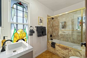Un baño con un lavamanos blanco, cabina de ducha con paredes de vidrio y un vitral.