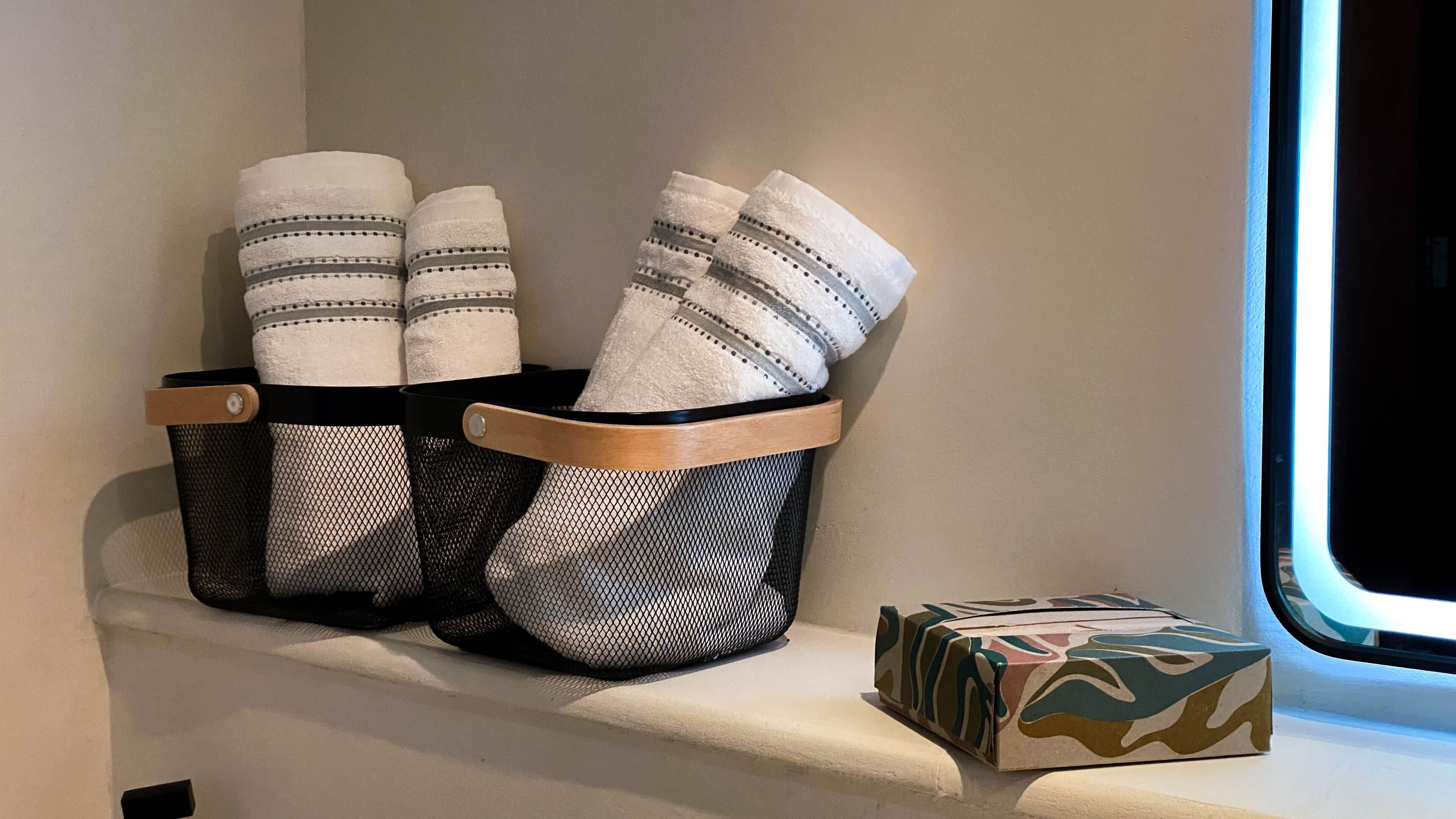 A window sill with two mesh baskets containing folded towels and a small box with a camouflage pattern.