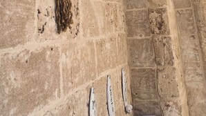 Una habitación con paredes de piedra, techo de bambú, una olla grande, una mesa de madera y una cesta.