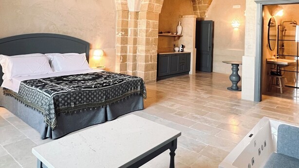 Una habitación amplia con cama, una mesa y zona de estar. Destacan paredes de ladrillo visto y un techo alto.