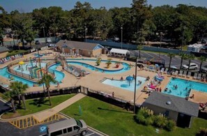 A large outdoor swimming pool with multiple lanes and a water slide, surrounded by lounge areas and palm trees. - Feet in the Sand Condo A-119 (Myrtle Beach)