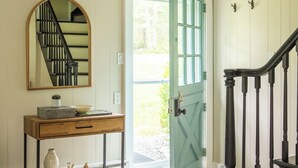 Un pasillo con una consola de madera, un espejo y una puerta verde que da a una escalera.