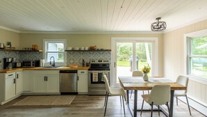 Una cocina con armarios blancos, encimera de madera, horno empotrado y comedor con mesa y sillas.