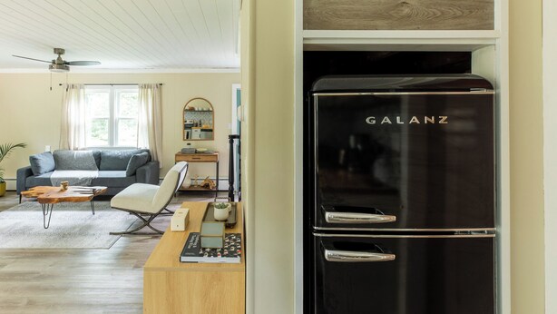 Una sala de estar moderna con un refrigerador Galanz negro, una mesa de centro de madera, un sofá gris y un ventilador de techo.