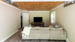 Una sala de estar con techo de madera, un sofá color beige, un televisor sobre un mueble de madera y una mesita.